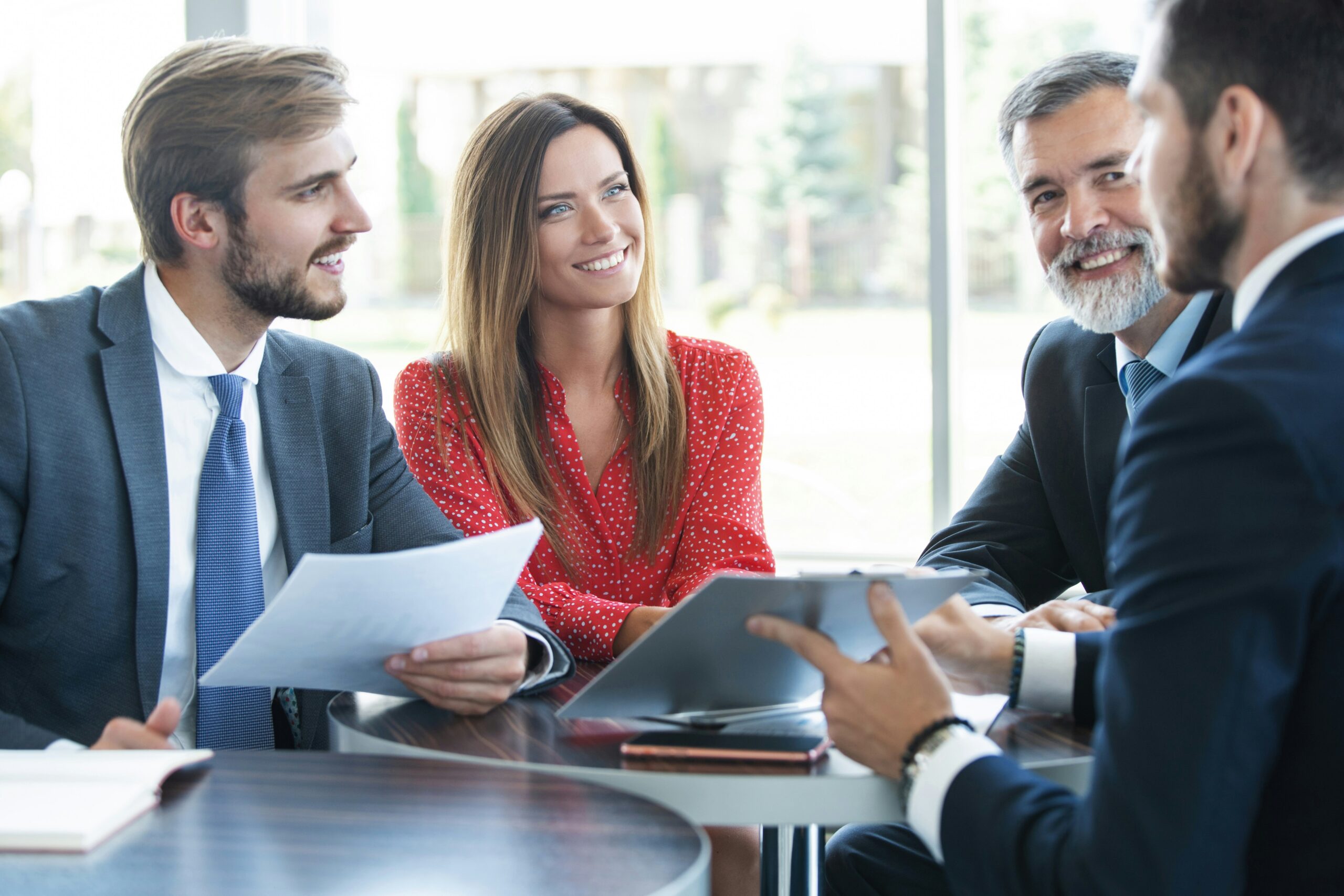 A financial advisor in a business suit smiles while reviewing documents across a table with a man and woman during a retirement planning consultation.